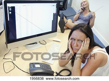 Stock Photo - an employee is disgruntled while a co-worker neglects work and talks on the phone; south shields tyne and wear england. Fotosearch