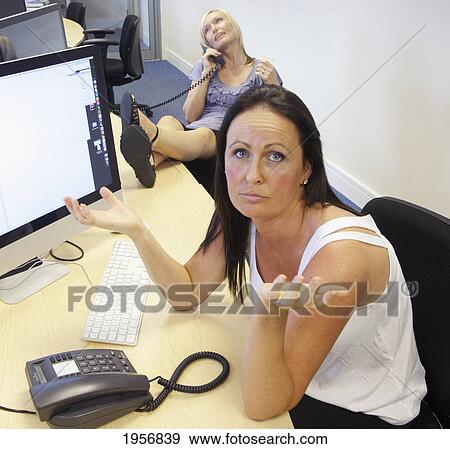 Stock Photo - an employee is frustrated while a co-worker neglects work and talks on the phone; south shields tyne and wear england. Fotosearch