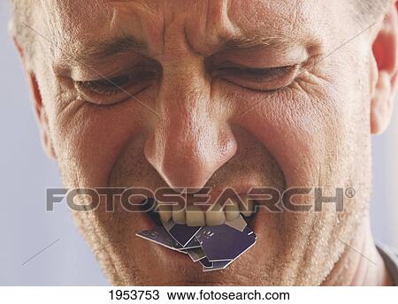 Stock Image - angry disappointed man with cut-up credit card in mouth; torremolinos malaga andalusia spain. Fotosearch