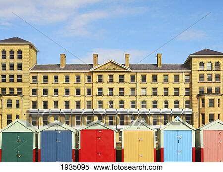 Stock Photography - Beach Huts Against Hotel; Brighton, East Sussex, England. Fotosearch