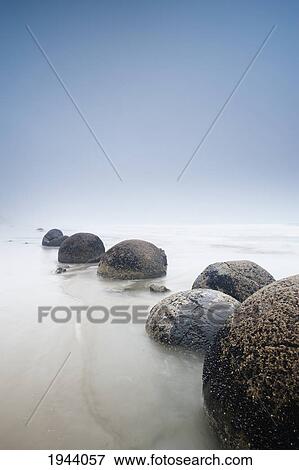 Boulders In A Row In The Shallow Water At The Beach Along The Coast; Moeraki South Island New Zealand View Large Photo Image Stock Photo - Boulders In A Row In The Shallow Water At The Beach Along The Coast; Moeraki South Island New Zealand. Fotosearch