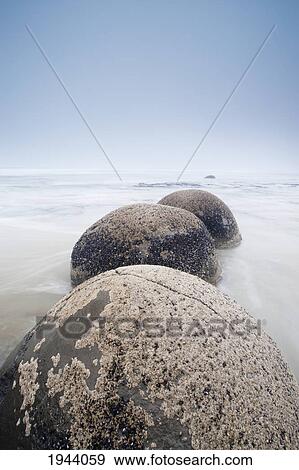 Stock Photo - Boulders In A Row In The Shallow Water Leading Out To The Ocean From The Beach; Moeraki South Island New Zealand. Fotosearch