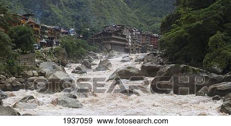 Stock Photo - Buildings In Machu Picchu Town On The Edge Of A Flowing River; Machu Picchu Peru. Fotosearch