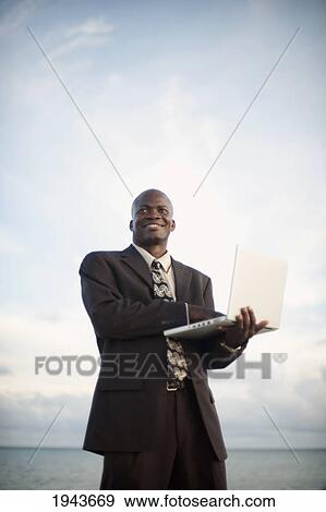 Businessman Working On A Laptop Computer By The Water's Edge; South Caicos Turks And Caicos Islands View Large Photo Image Stock Photo - Businessman Working On A Laptop Computer By The Water's Edge; South Caicos Turks And Caicos Islands. Fotosearch