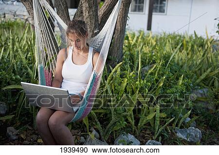 Stock Image - Girl Working On A Laptop While Sitting In A Hammock; South Caicos Turks And Caicos Islands. Fotosearch