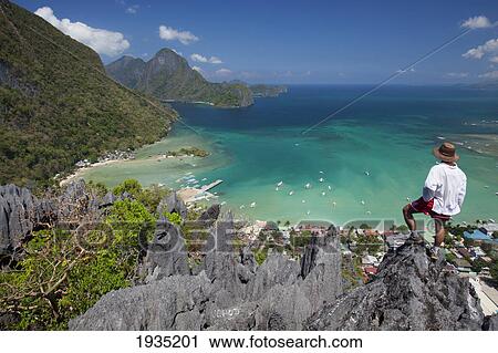 Man Enjoys View From Limestone Spires Over Coastal Village; El Nido, Palawan, Philippines View Large Photo Image Stock Image - Man Enjoys View From Limestone Spires Over Coastal Village; El Nido, Palawan, Philippines. Fotosearch
