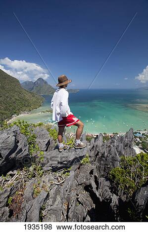 Man Enjoys View From Limestone Spires Over Coastal Village; El Nido, Palawan, Philippines View Large Photo Image Stock Photo - Man Enjoys View From Limestone Spires Over Coastal Village; El Nido, Palawan, Philippines. Fotosearch
