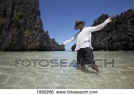 Stock Image - Man Standing In Clear Water Of Small Lagoon; Miniloc Island, Palawan, Philippines. Fotosearch