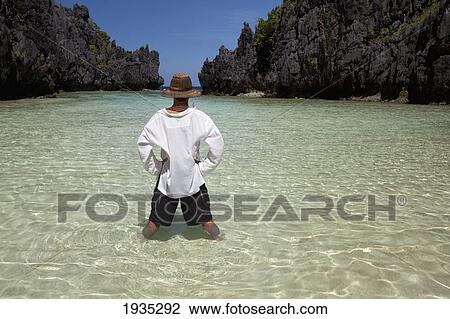 Stock Image - Man Standing In Clear Water Of Small Lagoon; Miniloc Island, Palawan, Philippines. Fotosearch