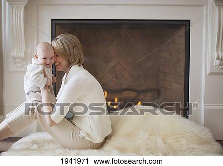 Stock Image - Mother And Baby Cuddling In Front Of Fireplace; Jordan Ontario Canada. Fotosearch