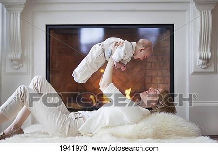 Stock Image - Mother And Baby On Carpet In Front Of Fireplace; Jordan Ontario Canada. Fotosearch