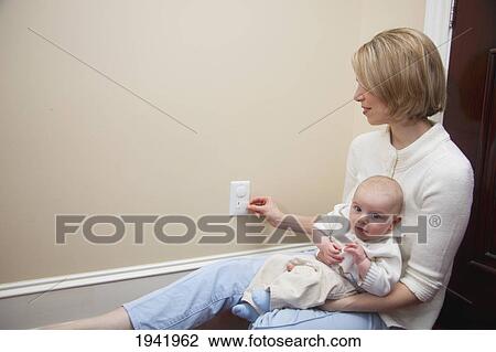 Stock Image - Mother With Baby Applying Safety Plug In Outlet; Jordan Ontario Canada. Fotosearch