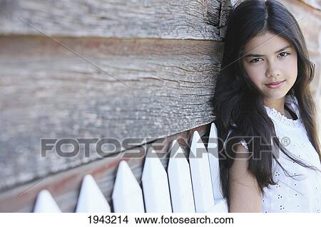 Picture - Portrait Of A Girl Leaning Against A Wooden Barn And A White Picket Fence; Troutdale Oregon United States Of America. Fotosearch