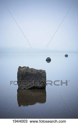 Stock Image - Rocks Reflected In The Tranquil Water; Iceland. Fotosearch