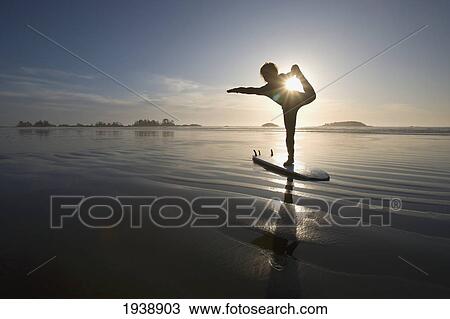Stock Image - Silhouette Of Female Surfer Doing Bow Pulling Yoga Pose; Chesterman Beach Tofino Vancouver Island British Columbia Canada. Fotosearch