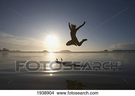 Silhouette Of Female Surfer Jumping For Joy; Chesterman Beach Tofino Vancouver Island British Columbia Canada View Large Photo Image Picture - Silhouette Of Female Surfer Jumping For Joy; Chesterman Beach Tofino Vancouver Island British Columbia Canada. Fotosearch