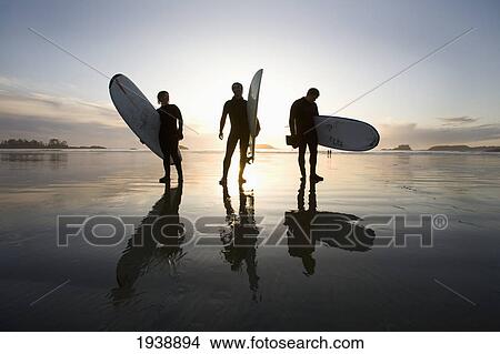 Picture - Silhouette Of Three Surfers Carrying Surfboards; Chesterman Beach Tofino Vancouver Island British Columbia Canada. Fotosearch