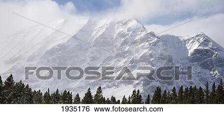 Stock Photograph - Snow-Capped Mountain Over Forest; Kananaskis Country, Alberta, Canada. Fotosearch