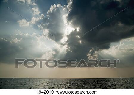 Stock Image - Sun Shining Through The Clouds; Phuket Thailand. Fotosearch