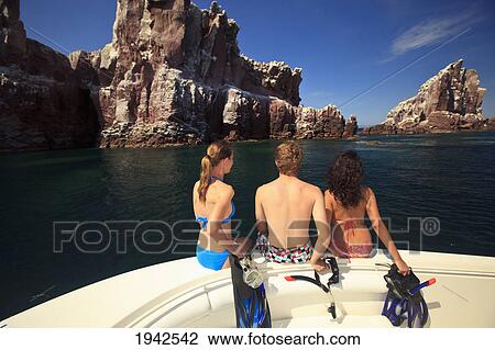 Stock Image - Three Tourists With Snorkeling Gear Sitting On The Edge Of A Boat At Los Islotes National Marine Park Espiritu Santo Island; La Paz Baja California Mexico. Fotosearch