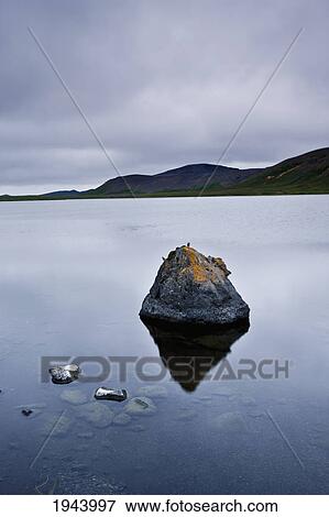 Stock Photo - Tranquil Scene With Rocks In The Water And Mountains Along The Shoreline; Iceland. Fotosearch