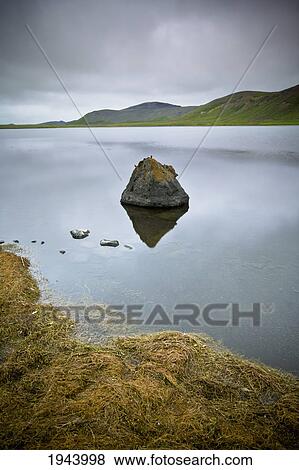 Stock Photo - Tranquil Scene With Rocks In The Water And Mountains Along The Shoreline; Iceland. Fotosearch