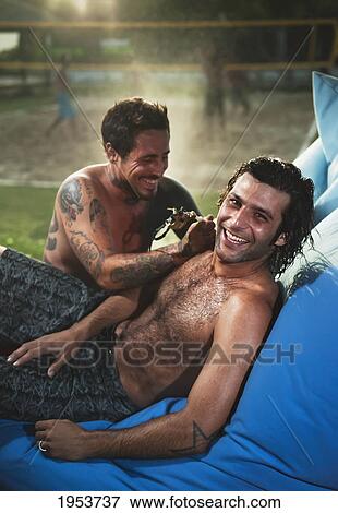 Stock Photo - two shirtless men laughing with a beach volleyball court in the background; tarifa cadiz andalusia spain. Fotosearch