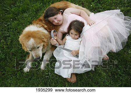 Stock Photo - Two Sisters In Dresses With Their Rescue Dog Outdoors; Duncan, Vancouver Island, British Columbia, Canada. Fotosearch