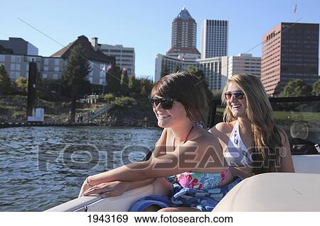 Stock Photo - Two Teenage Girls In Bathing Suits Riding In A Boat With The City In The Background; Portland Oregon United States Of America. Fotosearch