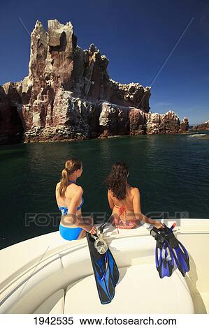 Stock Photography - Two Tourists Holding Snorkeling Gear As They Sit On The Edge Of A Boat At Los Islotes National Marine Park Espiritu Santo Island; La Paz Baja California Mexico. Fotosearch