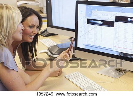 Stock Photo - two young woman looking at a cell phone while at work; south shields tyne and wear england. Fotosearch