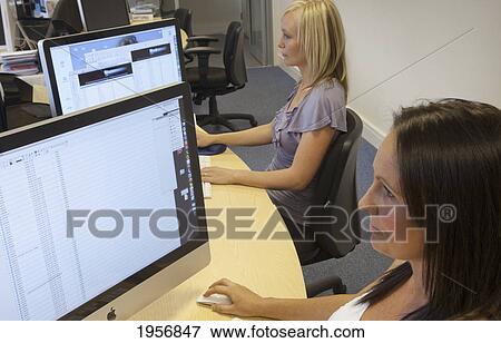 two young women sitting in front of their computer monitors at work; south shields tyne and wear england View Large Photo Image Stock Photo - two young women sitting in front of their computer monitors at work; south shields tyne and wear england. Fotosearch
