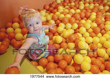 a baby girl plays in a pit full of orange and yellow balls; alberta canada View Large Photo Image Picture - a baby girl plays in a pit full of orange and yellow balls; alberta canada. Fotosearch