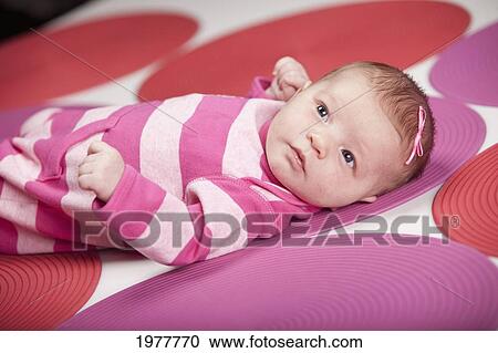 Stock Image - a baby girl wearing pink and white and laying on red and pink polka dots; edmonton alberta canada. Fotosearch