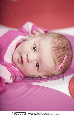 Stock Image - a baby girl wearing pink and white and laying on red and pink polka dots; edmonton alberta canada. Fotosearch