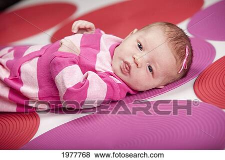 Stock Photo - a baby girl wearing pink and white and laying on red and pink polka dots; edmonton alberta canada. Fotosearch