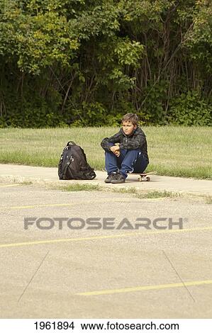 a boy sits on a skateboard with his backpack; edmonton, alberta, canada View Large Photo Image Picture - a boy sits on a skateboard with his backpack; edmonton, alberta, canada. Fotosearch