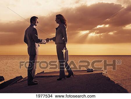 a businessman and businesswoman shaking in agreement on a dock along the water at sunset; tarifa cadiz andalusia spain View Large Photo Image Picture - a businessman and businesswoman shaking in agreement on a dock along the water at sunset; tarifa cadiz andalusia spain. Fotosearch