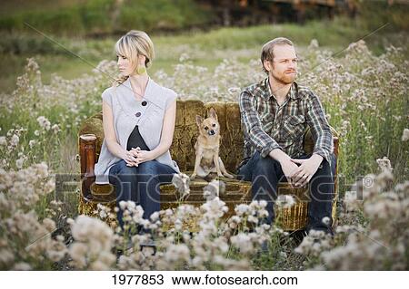 Stock Image - a couple sitting on opposite ends of a couch with a dog in between them; edmonton alberta canada. Fotosearch