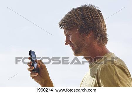 Picture - a man looking at the screen of his mobile phone; torremolinos, malaga, andalusia, spain. Fotosearch