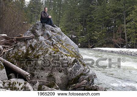 a man sits on a large rock elevated above the river flowing below in jasper national park; alberta canada View Large Photo Image Stock Photo - a man sits on a large rock elevated above the river flowing below in jasper national park; alberta canada. Fotosearch