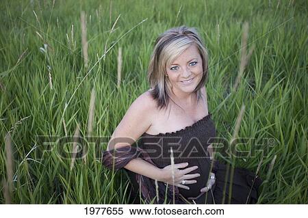 Stock Photography - a pregnant woman sits in the tall grass; edmonton alberta canada. Fotosearch