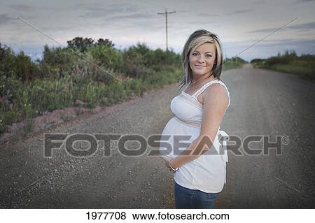 Stock Photo - a pregnant woman stands on a dirt road; edmonton alberta canada. Fotosearch