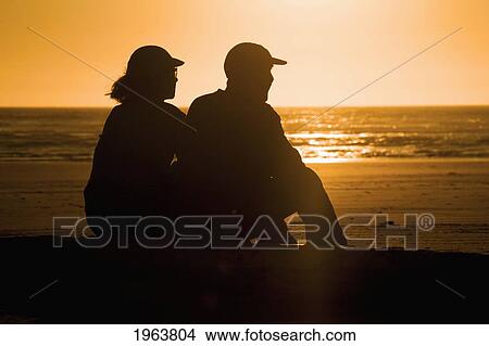 Picture - a silhouette of a couple sitting on a log on the beach at sunset; newport, oregon, united states of america. Fotosearch