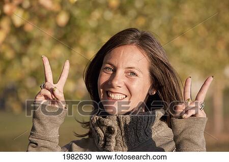 Stock Image - a woman giving a the peace symbol in a park in autumn; beaumont alberta canada. Fotosearch