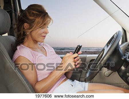 Stock Photograph - a woman sits in her car at dos mares beach using her cell phone; tarifa cadiz andalusia spain. Fotosearch