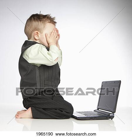 Stock Image - a young boy covers his eyes as he sits in front of a laptop computer; edmonton alberta canada. Fotosearch