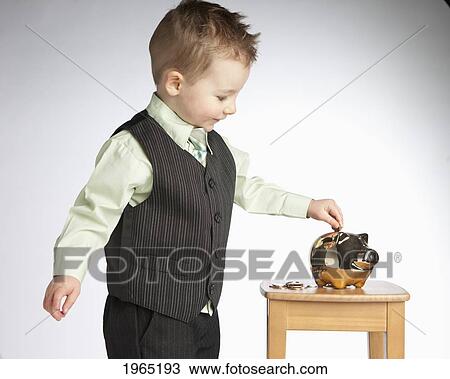 Stock Image - a young boy wearing a vest puts money into a piggy bank; edmonton alberta canada. Fotosearch