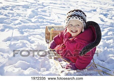 Stock Photography - a young girl in a pink snowsuit riding a toboggan through the snow; spruce grove alberta canada. Fotosearch