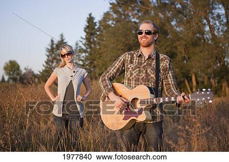 a young woman being ignored while standing in a field with a young man playing a guitar; edmonton alberta canada View Large Photo Image Stock Image - a young woman being ignored while standing in a field with a young man playing a guitar; edmonton alberta canada. Fotosearch